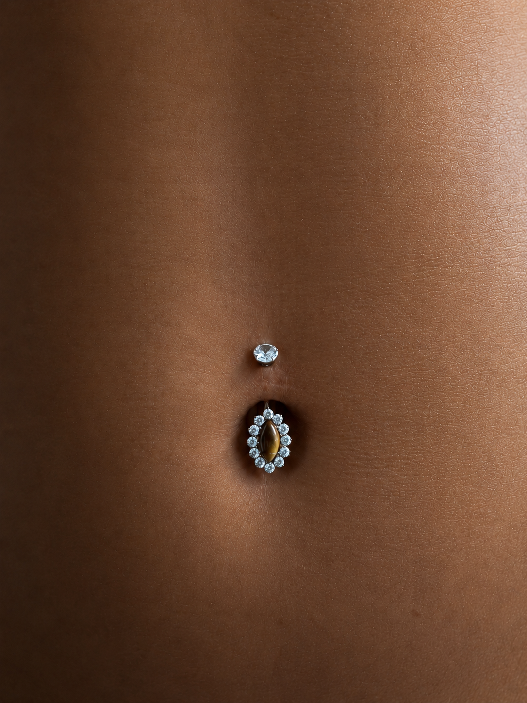 Piercing de nombril argenté avec pierre couleur œil-de-tigre entourée de zirconias.